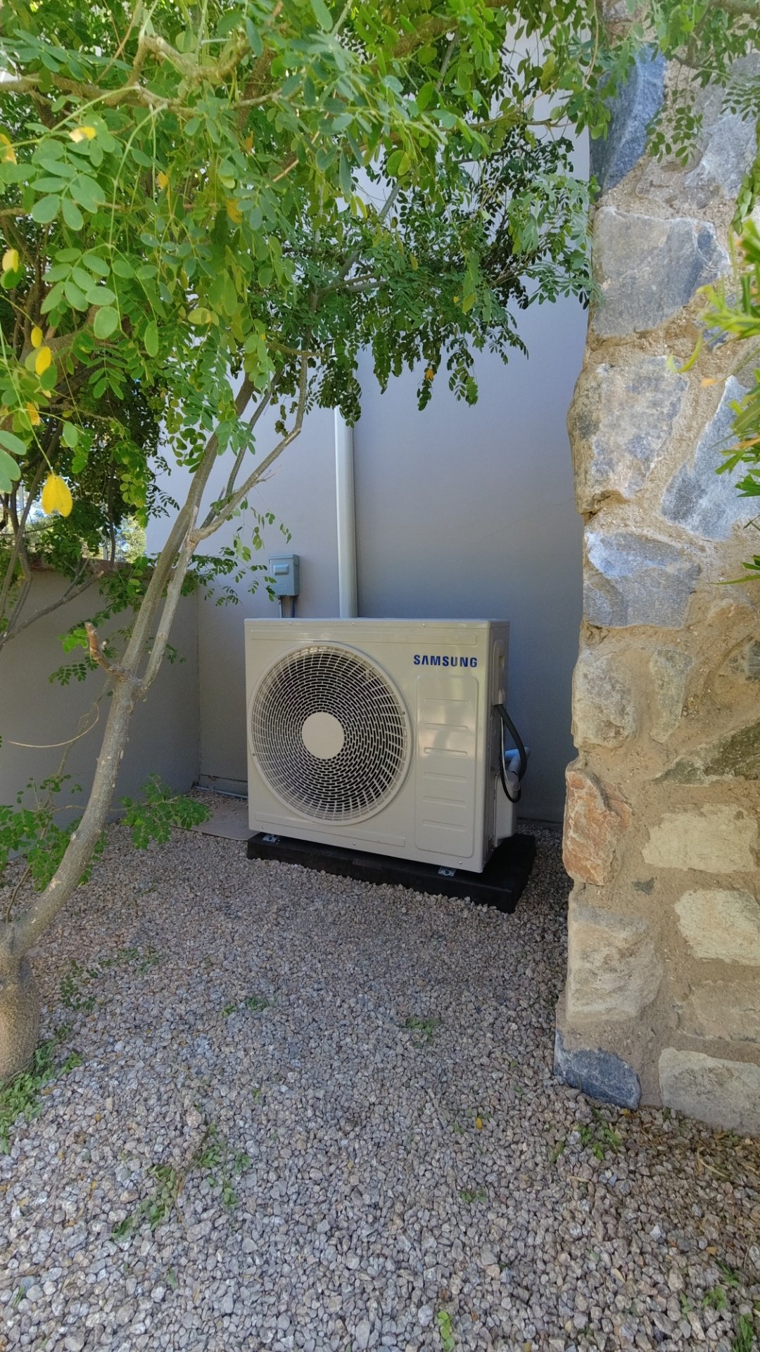 Samsung mini split outdoor condenser unit installed on gravel pad next to stone wall — real Mini Split Guys installation